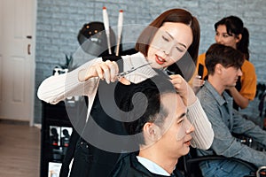 Qualified female barber make haircut for two male customer with male hairstyle.