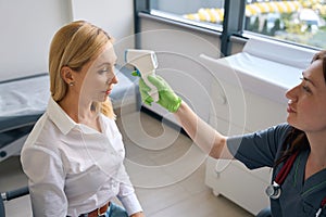 Qualified general practitioner measuring adult woman temperature