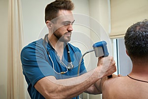 Qualified physical therapist is conducting ESWT procedure on adult man