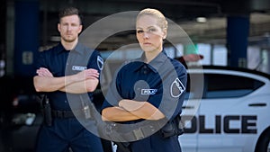 Qualified police officers posing on background of patrol car, criminal justice