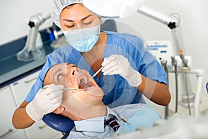 Qualified woman dentist in a protective mask treats a man patient