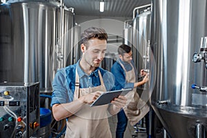 Quality control on brewery. Guys work near brewing kettles using tablet