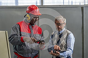 Quality Control Inspector Using Digital Tablet And Talking To African American CNC Machine Operator