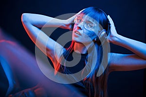 Quality music in headphones. Studio shot in dark studio with neon light. Portrait of young girl