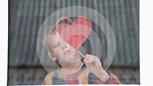 Quarantine. The boy draws red heart on the window with paint. Waiting for the rainbow, Stay home