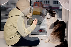 During the quarantine, a Child in a gas mask sits on the window. and the Maine Coon cat. He looks at the empty street. Apocalypse