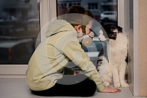 During the quarantine, a Child in a respirator sits on the window. and the Maine Coon cat. He looks at the empty street.