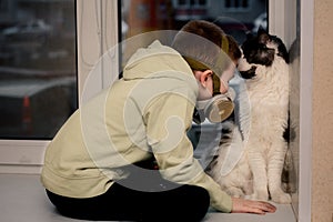 During the quarantine, a Child in a respirator sits on the window. and the Maine Coon cat. He looks at the empty street.