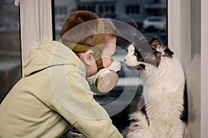 During the quarantine, a Child in a respirator sits on the window. and the Maine Coon cat. He looks at the empty street.