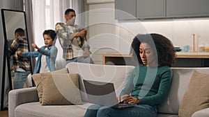 Quarantine family problems African American woman female mom trying to work online laptop pc sit sofa living room while