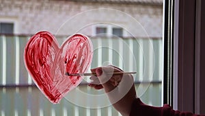 Quarantine. Female hand draws red heart on the window with paint. Waiting for the rainbow, Stay home