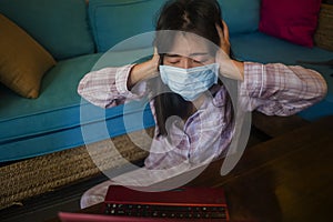 Quarantine and home lockdown - young beautiful scared and worried Asian Chinese woman on couch working or studying with laptop