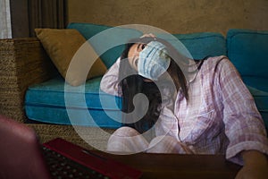 Quarantine and home lockdown - young beautiful scared and worried Asian Chinese woman on couch working or studying with laptop