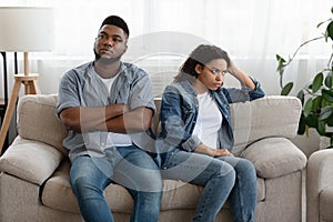 Quarantine Quarrels. African American Couple Ignoring Each Other After Arguing At Home, Sitting On Different Sides Of