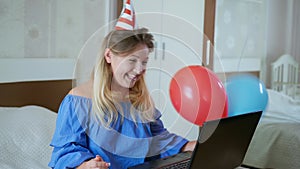 Quarantine self-isolation, young happy girl in cap with balloons and pipe congratulates her family on their birthday by