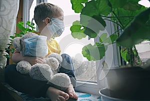 Quarantine, threat of coronavirus, virus protection, pandemic. Child and his teddy bear both in protective masks sits on