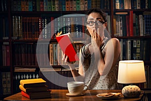 Quarantine. A young Caucasian woman with glasses reads a book with fright. The home library is in the background. The concept of