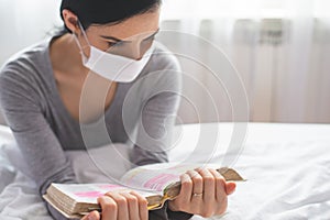 Quarantined woman with mask reading from bible and praying