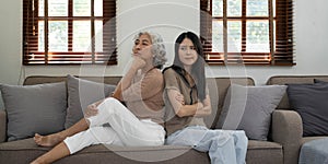 In quarrel elderly mother grown up daughter sit on couch separately having conflict, intergenerational misunderstanding