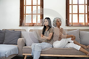 In quarrel elderly mother grown up daughter sit on couch separately having conflict, intergenerational misunderstanding