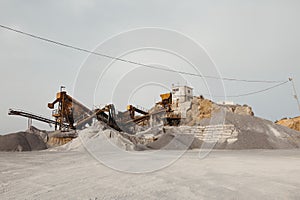 Quarry machines and piles of gravel over blue sky. Stone crushing and screening plant