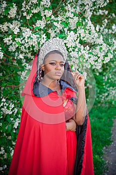 Queen in the crown and royal mantle. Lovely girl on the background of a blooming garden. African