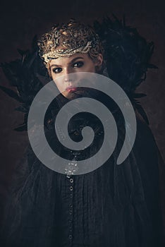 Queen of darkness in black fantasy costume on dark gothic background. High fashion beauty model with dark makeup.