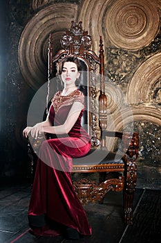 Queen in red dress sitting on throne. Symbol of power