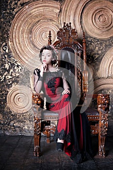 Queen in red dress sitting on throne. Symbol of power and wealth