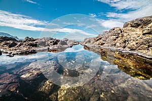 Queen`s Bath on Kauai, Hawaii island. Ocean pond in rocks with sky reflection