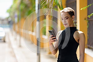 Queer non-binary man with mustache wearing lipstick and jumpsuit using mobile phone outdoors photo