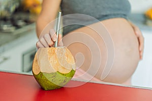 Quenching her pregnancy thirst with a refreshing choice, a pregnant woman joyfully drinks coconut water from a coconut