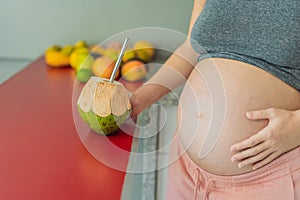 Quenching her pregnancy thirst with a refreshing choice, a pregnant woman joyfully drinks coconut water from a coconut