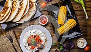 Quesadilla, salad with cottage cheese and tomatoes, two corn on wood table.