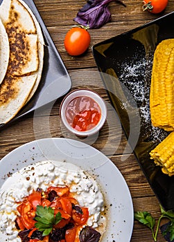 Quesadilla, salad with cottage cheese and tomatoes, two corn on wood table.