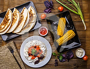 Quesadilla, salad with cottage cheese and tomatoes, two corn on wood table.