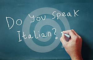 The question do you speak italian written on chalkboard and male hand