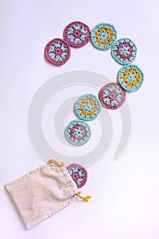 Question mark made of circle crochet motifs with a dot coming out of a cloth bag on white background