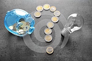 Question mark made of coins, piggy bank and light bulb on grey background. Electricity saving concept