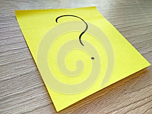 Question mark message on yellow sticky note on wooden background