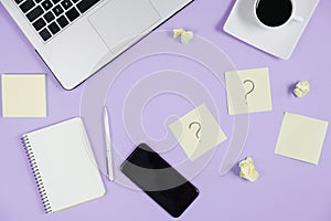 Question mark on sticky notes, notebook, laptop, cup coffee, phone, pen on violet background. FAQ concept. Working with clients.