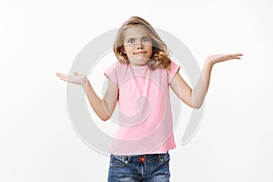 Questioned cute funny young child, girl shrugging and pursing lips stare camera unaware and clueless, shaking head