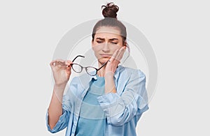 Questioned pretty young woman has thinking expression, looking through her transparent eyeglasses. Doubtful girl wears eyewear can