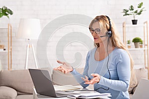 Questions in online meeting at home. Woman with headset gesticulation and answering online photo