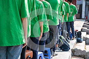 Queue of Asian teenagers in green t-shirt uniform standing in line