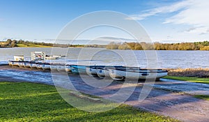 A queue of rowing boats on the shoreline of Pitsford Reservoir, UK