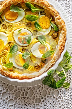 Quiche with with boiled eggs and leeks sprinkled with fresh lambs lettuce served in casserole dish on a white table