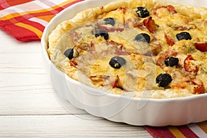 Quiche with ham, cheese, tomatoes and black olives on the wooden background.