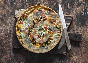 Quiche with kale, chicken, zucchini, sweet pepper, ham, mozzarella cheese on a wooden cutting board, top view. Delicious snack,