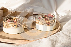 Quick healthy breakfast greek yogurt, granola with dried berries and nuts in glass jar on wooden tray on white bedding